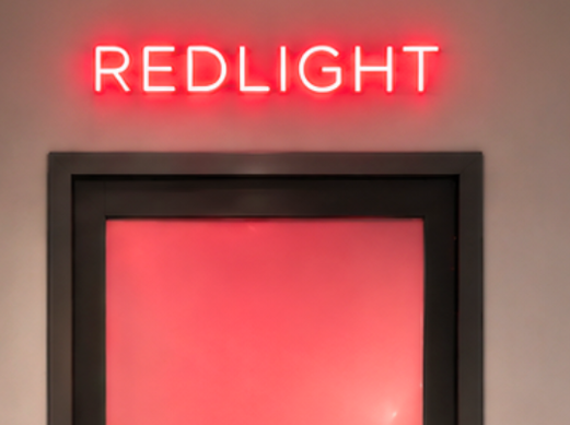 Entrance to a dedicated red light therapy room featuring a glowing frosted glass door and modern wellness studio design focused on recovery and rejuvenation